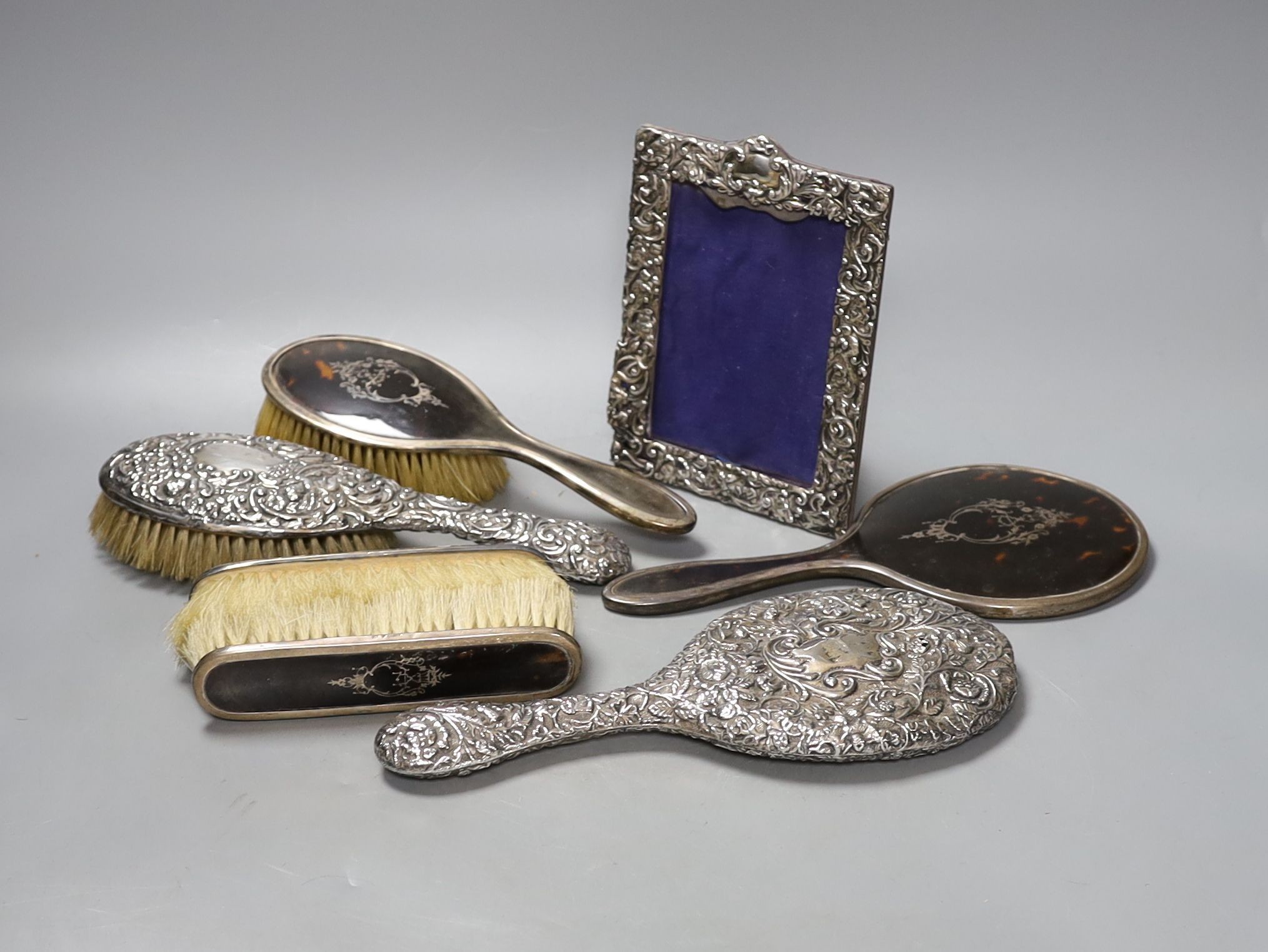 A George V silver and tortoiseshell mounted brush set and a tow similar embossed silver items(a.f.) and a silver mounted photograph frame.